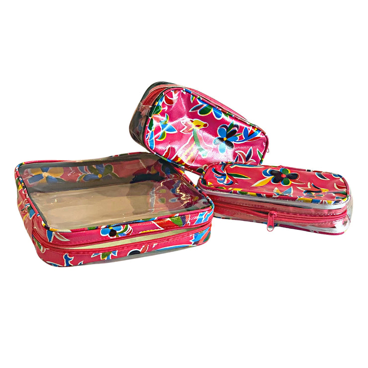 Above view: One large and two small travel cases, multi-colored flower/animal print on pink background.
