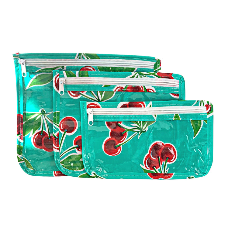 Front view: Small, medium and large slim travel bags, white zippers and cherry print on green background.