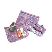 Above view: Small, medium and large slim travel bags, pink zippers and pink, blue and purple splatter print, showing travel items through transparent font. 