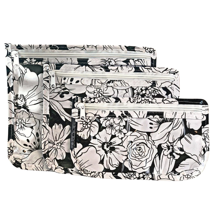 Front view: Small, medium and large slim travel bags, white zippers and white floral print on a black background.