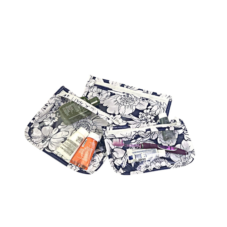 Above view: Small, medium and large slim travel bags, white zippers and white floral print on a blue background, showing travel items through transparent front.