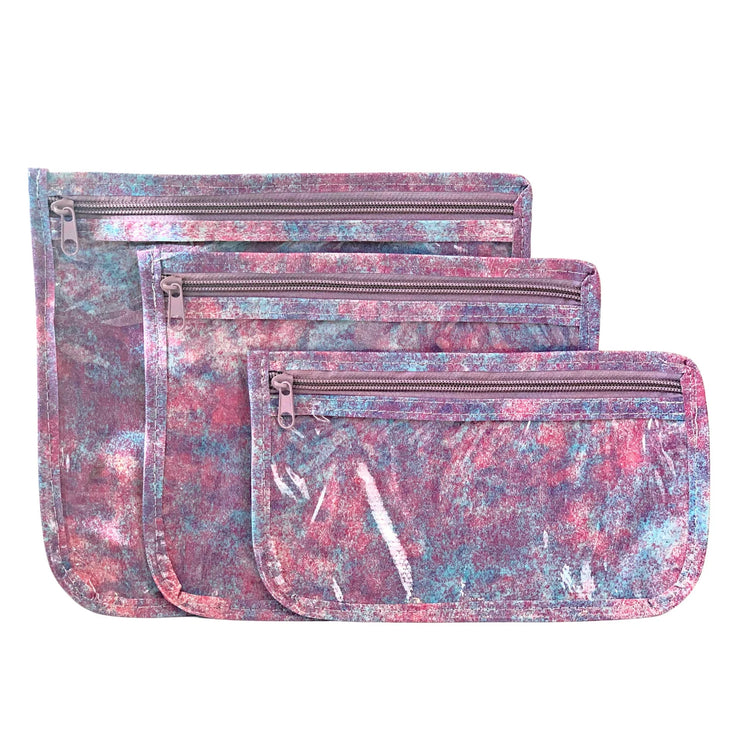 Front view:   Small, medium and large slim travel bags, pink zippers and pink, blue and purple splatter print. 