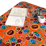 Above view: Multi-colored floral print on terracotta background tablecloth covering table, with open notebook displayed. 