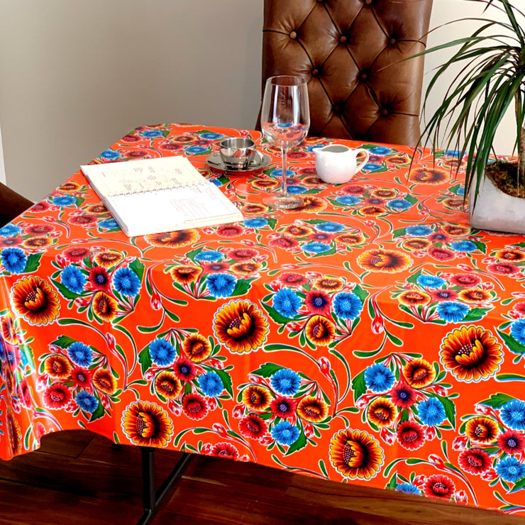 Above view: Multi-colored floral print on terracotta background tablecloth covering table, with opened notebook displayed.