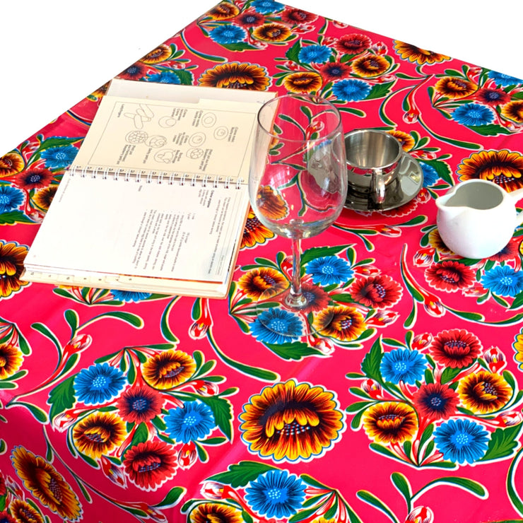 Above view: Multi-colored floral print on pink background tablecloth covering table, with opened notebook displayed.