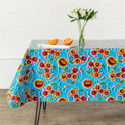 Side view:  Multi-colored floral print on light blue background tablecloth covering table, with lilies centerpiece. 