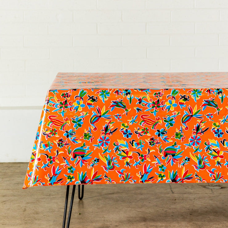 Side view: Multi-colored animal/floral print on orange background tablecloth covering table.