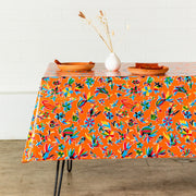 Side view: Multi-colored animal/floral print on orange background tablecloth covering table, with place settings and dried grass centerpiece.