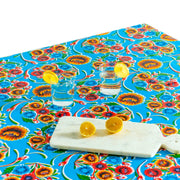 Above view:  Multi-colored floral print on light blue background tablecloth covering table, with orange fruit platter as centerpiece. 