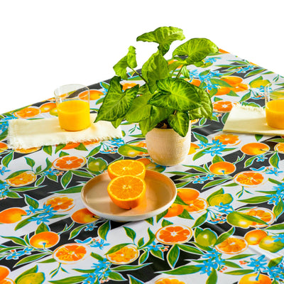 Above view: Orange fruit print on black and white background tablecloth covering table, with potted plant centerpiece.