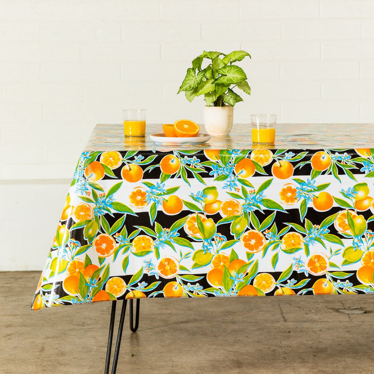 Side view: Orange fruit print on black and white background tablecloth covering table, with potted plant centerpiece.