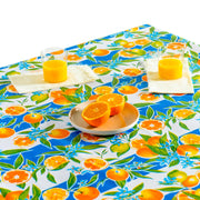 Above view: Orange fruit print on blue and white background tablecloth covering table, with plate of oranges.