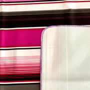 Close up: Multi-colored vertical striped patterned tablecloth with white underside folded up to show contrast.