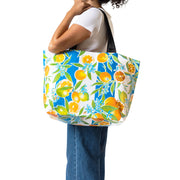 Front view: Woman models orange fruit print on blue and white vertical striped background tote with black handles.