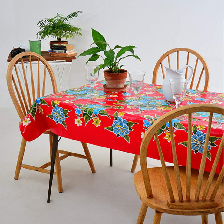 Side view: Multi-colored hibiscus print on red background tablecloth covering table, with potted plant centerpiece.