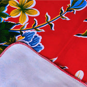 Close up: Multi-colored hibiscus print on red background tablecloth, white underside folded up to show contrast.