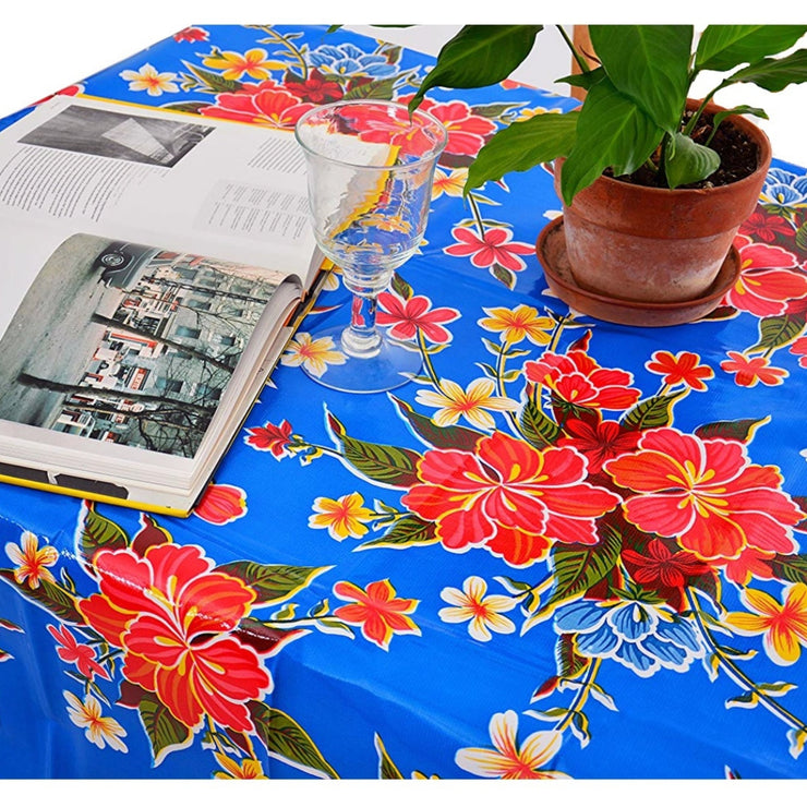 Above view: Multi-colored hibiscus print on blue background tablecloth covering table, with open book displayed and potted plant centerpiece.