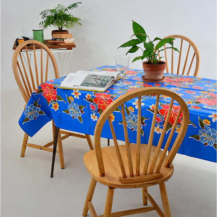 Side view: Multi-colored hibiscus print on blue background tablecloth covering table, open book displayed and potted plant centerpiece.