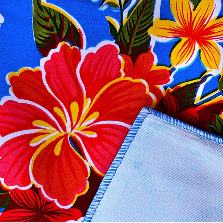 Close up: Multi-colored hibiscus print on blue background tablecloth, white underside folded up to show contrast.