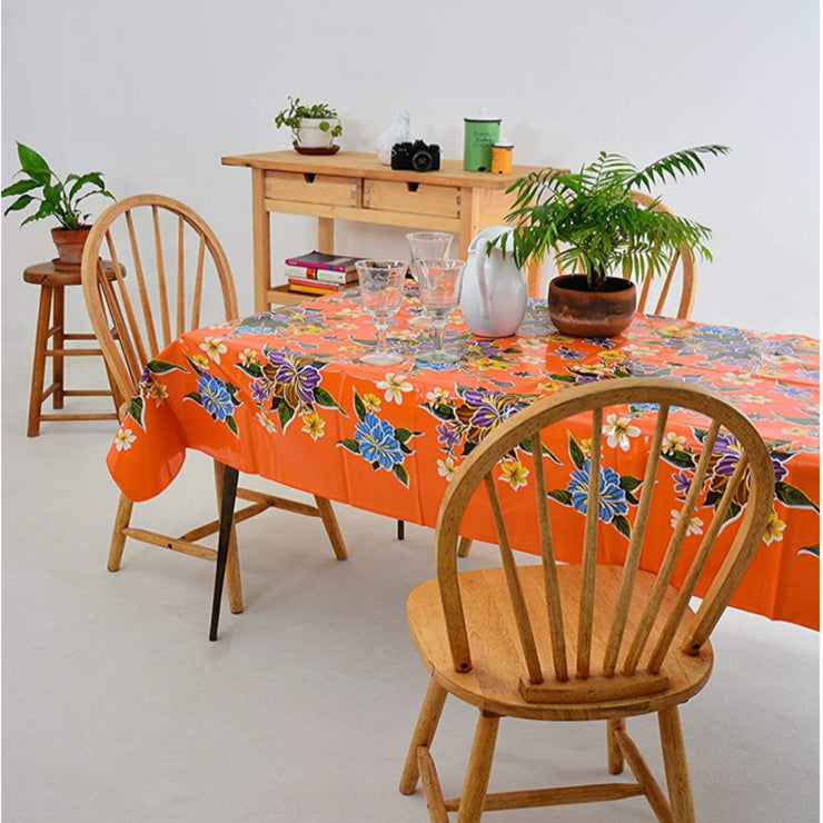 Side view: Multi-colored hibiscus print on orange background tablecloth covering table with potted plant centerpiece.