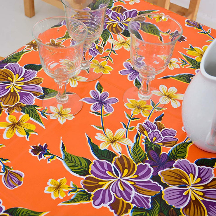 Above view: Multi-colored hibiscus print on orange background tablecloth covering table.