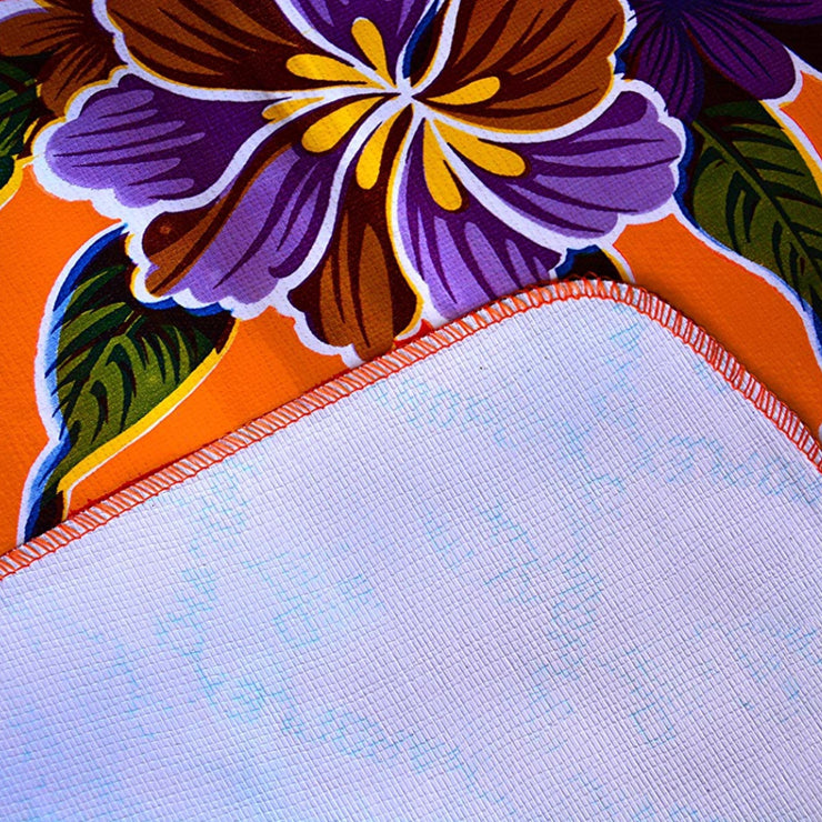 Close up" Multi-colored hibiscus print on orange background tablecloth, white underside folded up to show contrast.