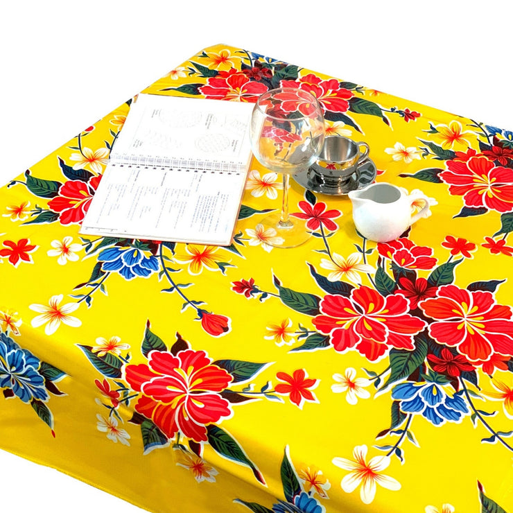 Above view: Multi-colored hibiscus print on yellow background tablecloth covering table, open notebook displayed.