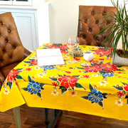 Side view: Multi-colored hibiscus print on yellow background tablecloth covering table, open notebook displayed and potted plant centerpiece.