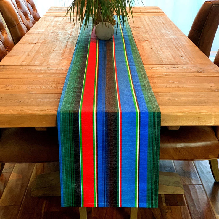 Above view: Multi-colored vertical striped patterned table runner on wooden table, shown with plant centerpiece.