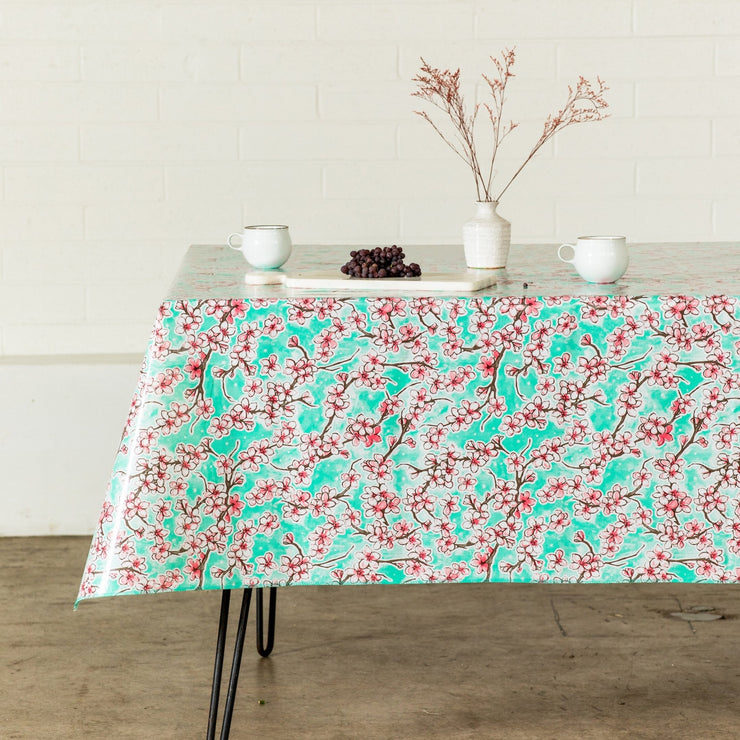 Side view: Cherry blossom print on mint green background tablecloth covering table with platters of grapes and dried grass centerpiece.