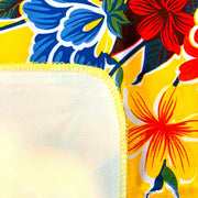 Close up: Multi-colored hibiscus print on yellow background tablecloth, white underside folded up to show contrast.