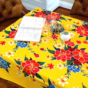 Above view: Multi-colored hibiscus print on yellow background tablecloth covering table, open notebook displayed.