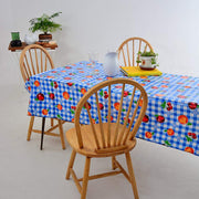 Angled view: Fruit print on blue and white checkered background tablecloth covering table, with potted plant centerpiece.