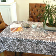 Above view: Black floral print on white background tablecloth covering table, open notebook displayed. 