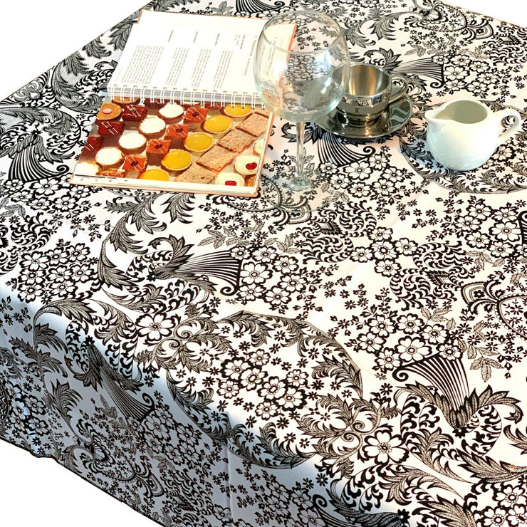 Above view:  Black floral print on white background tablecloth covering table, open notebook displayed.