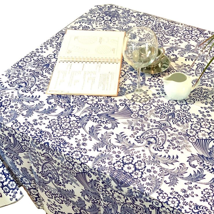 Above view: Blue floral print on white background tablecloth covering table, open notebook displayed.