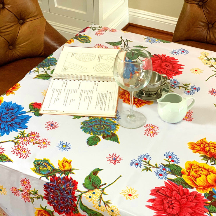 Above view:  Multi-colored floral print on white background tablecloth, covering table, with open notebook displayed.