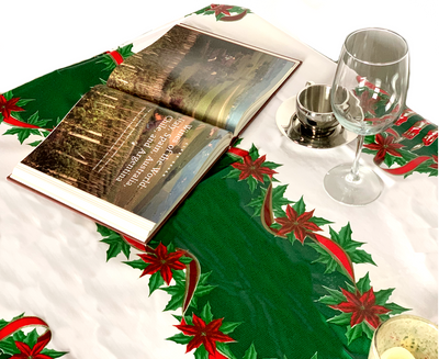 Above view: Green ribbons with poinsettia edging on white background tablecloth, open book displayed.  