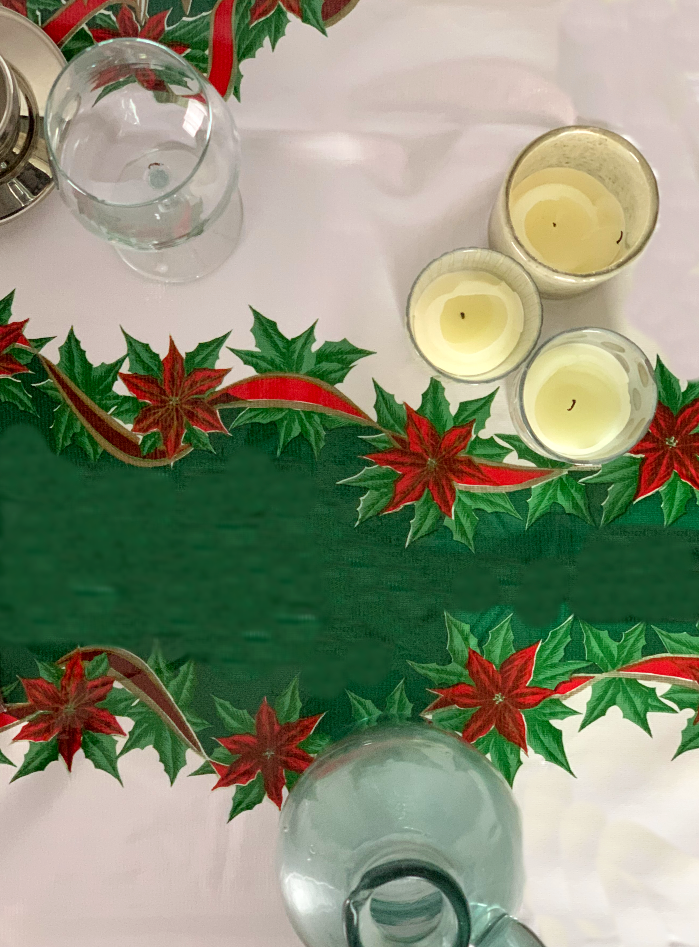 Above view: Green ribbons with poinsettia edging on white background tablecloth, candles displayed.