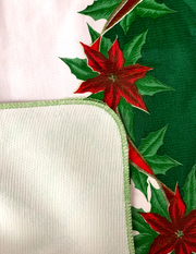 Close up: Green ribbons with poinsettia edging on white background tablecloth with white underside folded up to show contrast. 