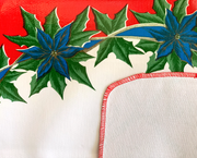 Close up: Blue ribbons with poinsettia edging on white and red striped background tablecloth with white underside folded up for contrast. 