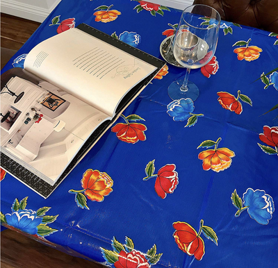 Above view: Multi-colored flower print on blue background tablecloth, opened book displayed.