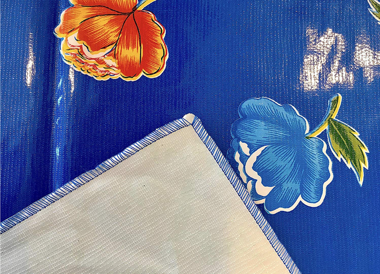 Close up: Multi-colored flower print on blue background tablecloth, with white underside folded up to show contrast.