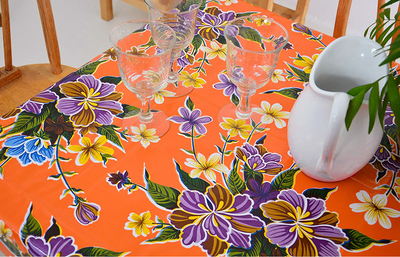 Above view: Multi-colored floral print on orange background tablecloth, with potted plant centerpiece.