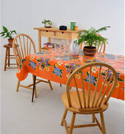 Angle view: Multi-colored floral print on orange background tablecloth, with potted plant centerpiece.