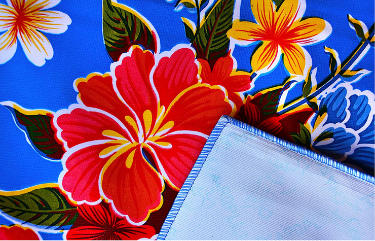 Close up: Multi-colored floral print on blue background tablecloth with white underside folded up to show contrast.