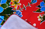 Close up: Multi-colored floral print on red background tablecloth with white underside folded up to show contrast.