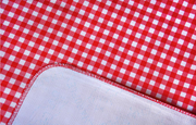 Close up: Red and white checkered pattern tablecloth with white underside folded up to show contrast. 