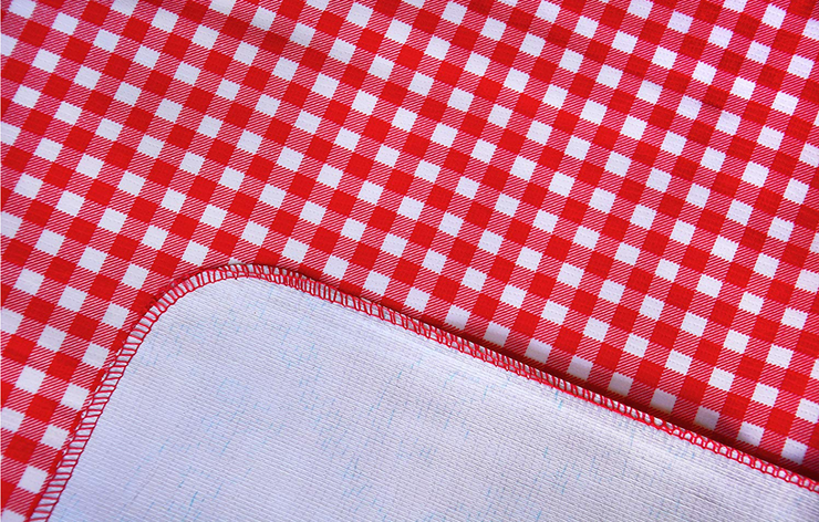 Close up: Red and white checkered pattern tablecloth with white underside folded up to show contrast. 