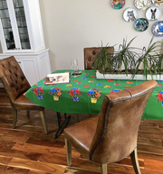 Angle view: Multi-colored flower print on green background tablecloth, open book displayed with potted plant centerpiece.